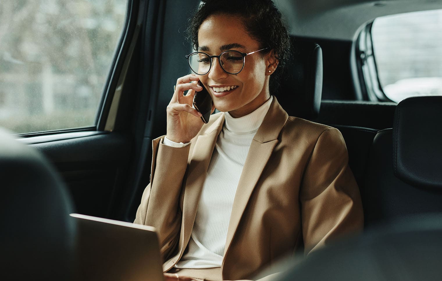 Frau ist im Auto am telefonieren und schaut auf ein Laptop