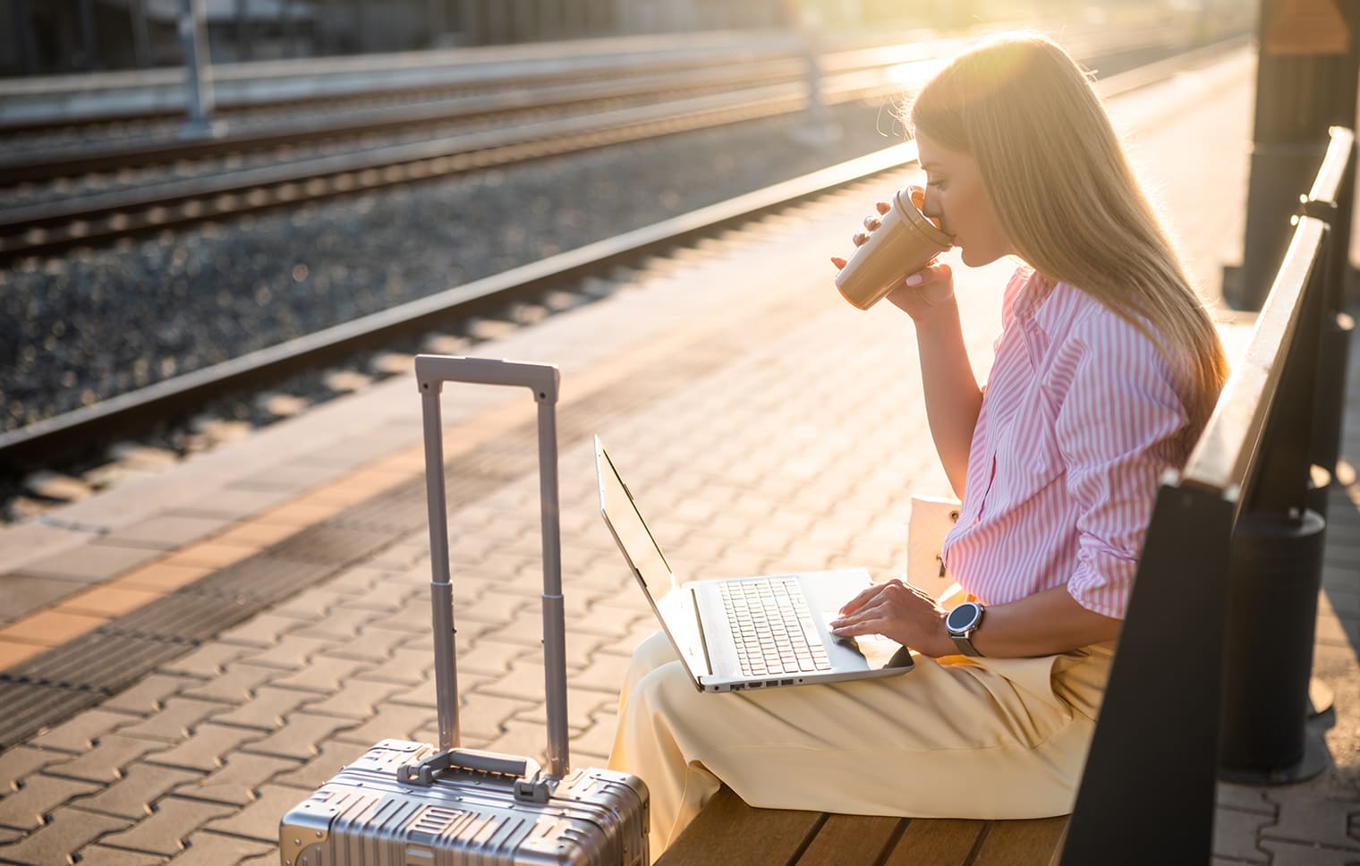 Frau sitzt am Bahnsteig mit einem Kaffee